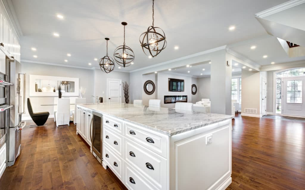 Remodeled kitchen with wood floors, white cabinets, large island, and marble countertops. Recessed and pendant lighting.