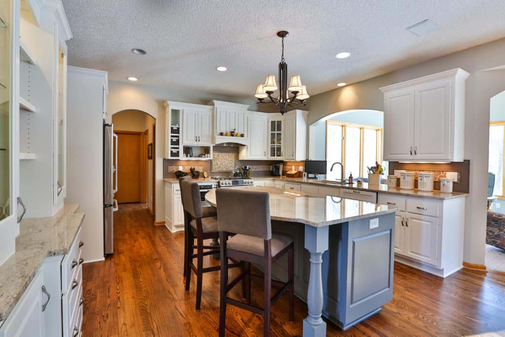 Remodeled kitchen with a custom blue kitchen island with seating. Stone countertops. Wood flooring. White cabinets.