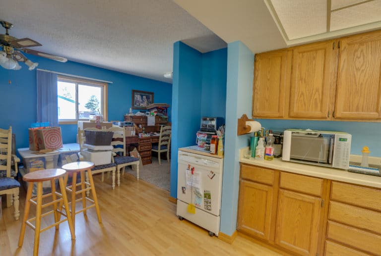 Kitchen before with blue walls, outdated wood cabinetry, and carpet in the living area with a wall separating the two.