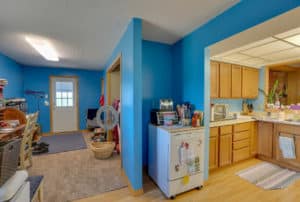 Kitchen before with blue walls, outdated wood cabinetry, and carpet in the living area with a wall separating the two.