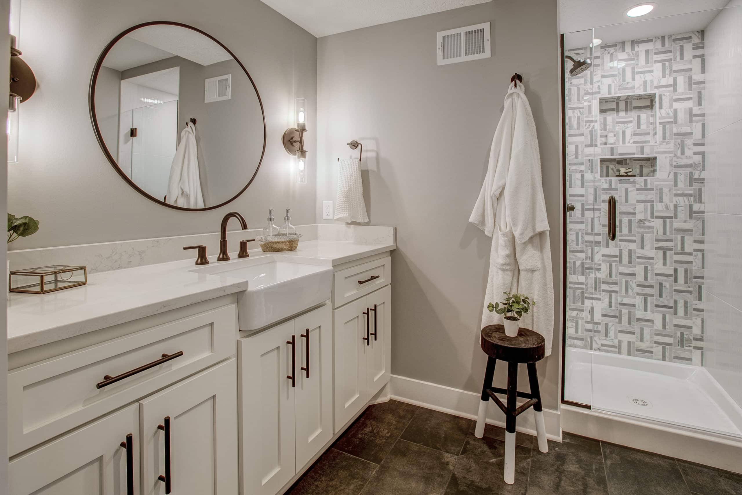 Remodeled bathroom with dual white sinks, with round mirror centered, and gold trim