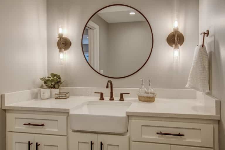 Remodeled bathroom with dual white sinks, with round mirror centered, and gold trim
