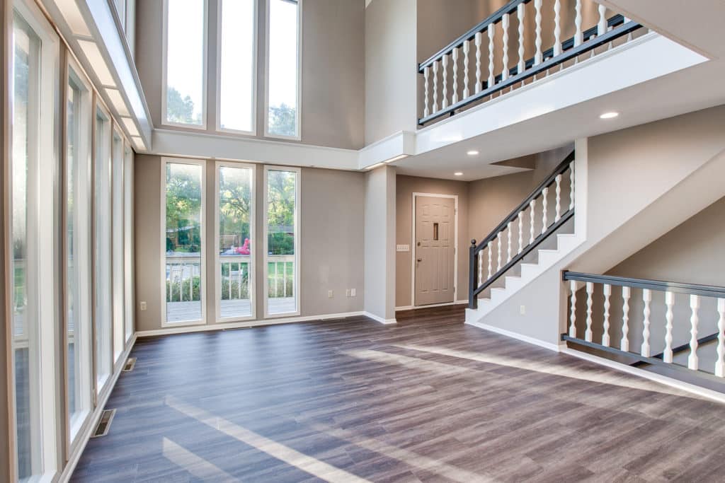 Living room with luxury vinyl flooring installed. View of two floors' worth of tall windows and a staircase and upper level railing.