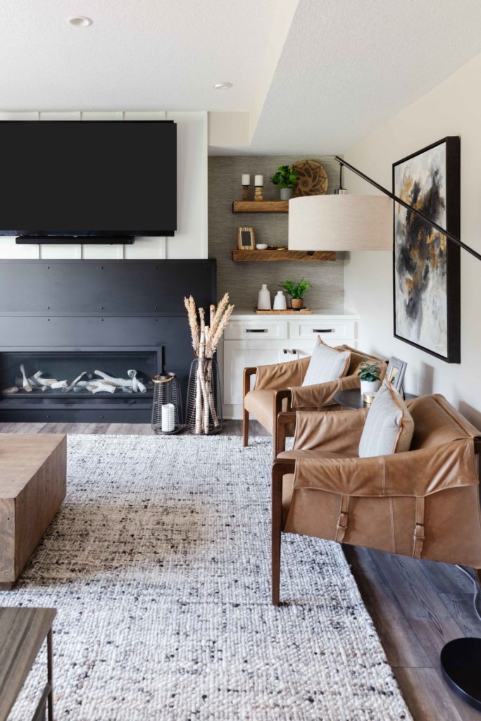 Remodeled living area with built in modern electric fireplace, large gray area rug, and brown furniture